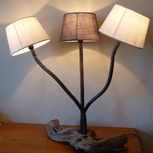 Lamp bestaande uit een basis van drijfhout, gelakte, zeeroestende metalen staven en drie stoffen lampenkappen, 2 witte en 1 taupe