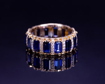 May include: A gold band ring featuring a series of alternating rectangular baguette-cut deep blue sapphires and small round clear diamonds set in a continuous pattern around the entire circumference of the metal band.