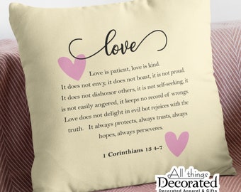 May include: A beige throw pillow with a pink heart and the text "love" in a cursive font. The pillow features a quote about love from 1 Corinthians 13:4-7.