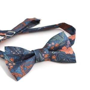 Könnte beinhalten: Eine blaue Fliege mit einem floralen Muster in Orange- und Rosatönen. Die Fliege hat einen verstellbaren Riemen.