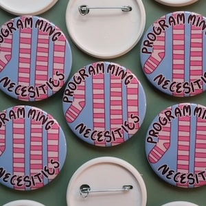 May include: Ten blue and white striped pins with the text "Programming Necessities" in white lettering. The pins are circular and have a shiny finish.