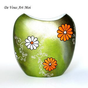 Peut inclure: Vase vert avec un motif floral orange et blanc. Le vase a une finition métallique avec un dessus incurvé et est décoré de vignes blanches tourbillonnantes. Le texte "De Vous Art Moi" est visible en haut à gauche.