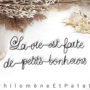 Peut inclure: Une décoration murale en fil de fer noir formant le texte cursif La vie est faite de petits bonheurs. L'écriture est réalisée à partir d'un seul fil métallique continu, créant un rendu épuré. Le texte est disposé sur deux lignes distinctes.