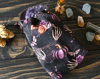 May include: A black drawstring bag with a spooky Halloween print featuring pumpkins, skeletons, and butterflies. The bag is made of fabric and has a drawstring closure.