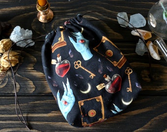 May include: A black drawstring bag with a repeating pattern of blue hands, keys, potion bottles, and books. The bag is made of fabric and has a drawstring closure.