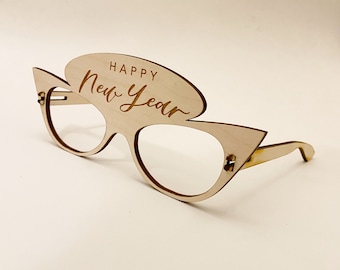 Puede incluir: Gafas de madera con la inscripción "Happy New Year". Las gafas son de color marrón claro y tienen forma de ojo de gato.