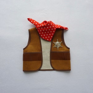 May include: A brown suede vest with fringe detail and a silver sheriff's star badge. A red bandana with white stars is draped over the vest.