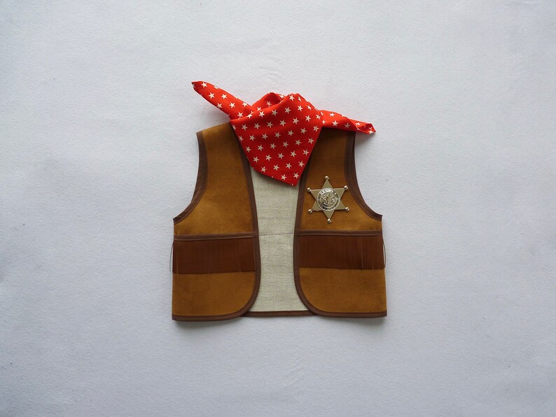 May include: A brown suede vest with fringe detail and a silver sheriff's star badge. A red bandana with white stars is draped over the vest.