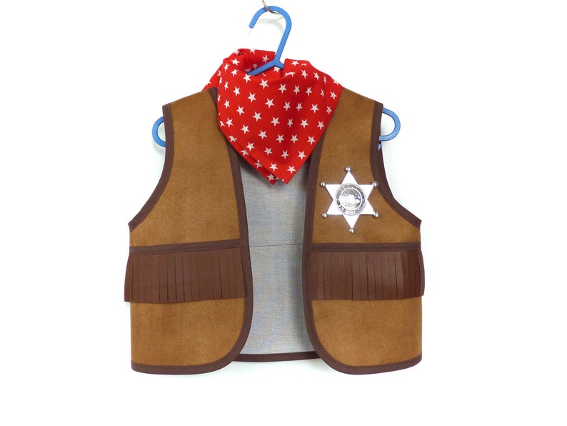 May include: A brown suede vest with fringe detailing, a red bandana with white stars, and a silver sheriff's badge.