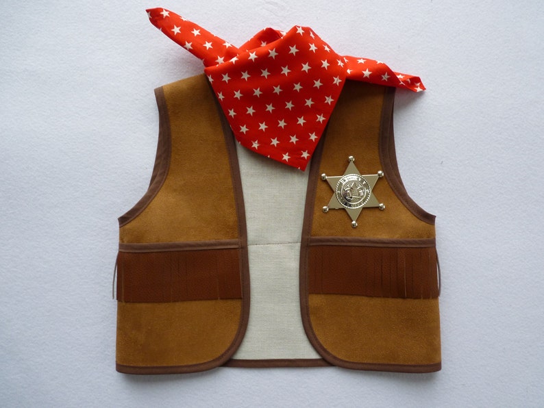 May include: A brown suede vest with fringe detailing, a silver sheriff's badge, and a red bandana with white stars.