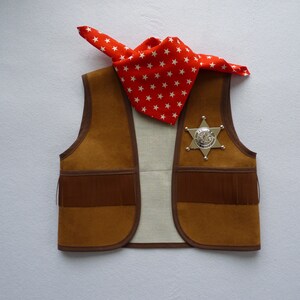 May include: A brown suede vest with fringe detailing and a silver sheriff's star badge. A red bandana with white stars is draped over the vest.