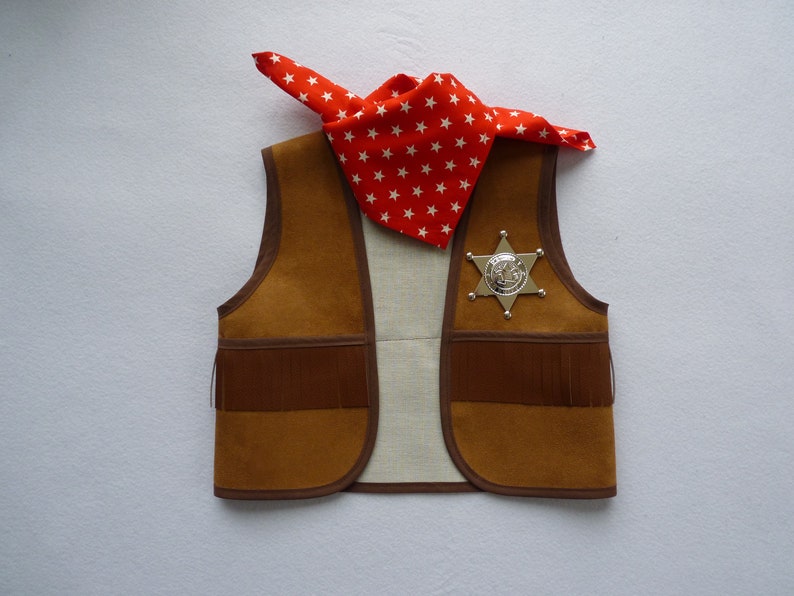 May include: A brown suede vest with fringe detailing and a silver sheriff's star badge. A red bandana with white stars is draped over the vest.