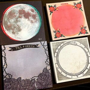 May include: Four square notepads with unique designs. One features a 3D moon with red and green accents, another has a pink circle with roses and the text "LOVE WITCH". The third has the text "TILL DEATH" and roses. The last has a snake eating its tail.