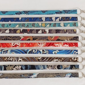 Peut inclure: Dix lanières en tissu colorées avec des fermoirs en métal argenté. Les lanières présentent différents motifs, notamment des nuages, des vagues et des motifs géométriques. Les lanières sont numérotées de 1 à 10.