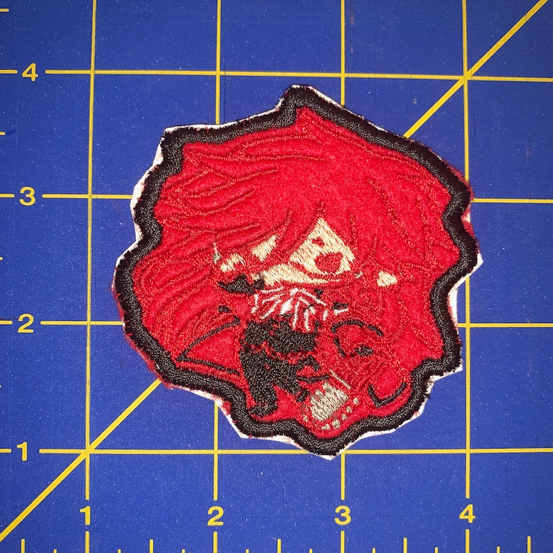 May include: Embroidered iron-on patch featuring a cartoon character with red hair, black eyes, and a red and black outfit. The character is smiling and holding a red heart.