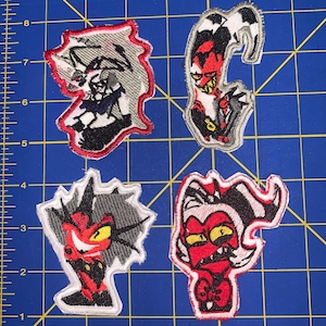 May include: Four embroidered iron-on patches featuring cartoon characters with red, black, and white details. The characters have horns, fangs, and angry expressions.