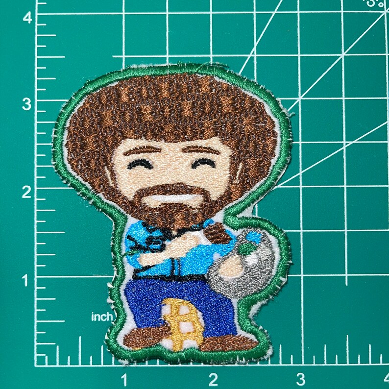 May include: Embroidered patch featuring a cartoon illustration of Bob Ross, known for his popular television show "The Joy of Painting". The patch depicts Bob Ross with his signature afro hairstyle, a blue shirt, and a paint palette in his hand. The patch is surrounded by a green border.