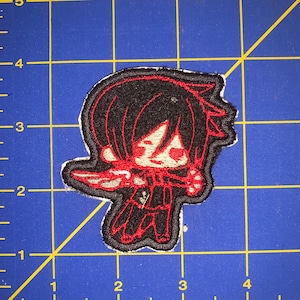 May include: Embroidered patch featuring a cartoon character with black hair, red eyes, and a red and black outfit. The character is holding a red object in their right hand.