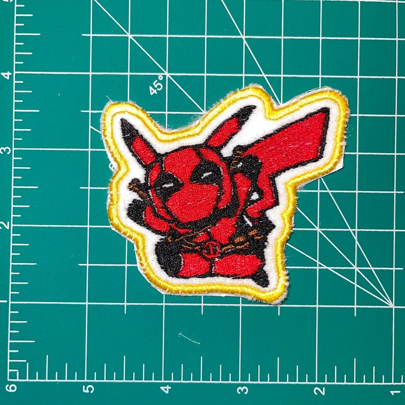 May include: Embroidered patch featuring a red and black cartoon character with a yellow outline. The character is wearing a red and black suit with a chain around its neck. The character is in a pose similar to the Pokemon character Pikachu.