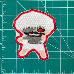 May include: White and red embroidered patch of a cartoon character with spiky white hair, a red eye, and a black and grey face. The character is wearing a white shirt and has a red outline.
