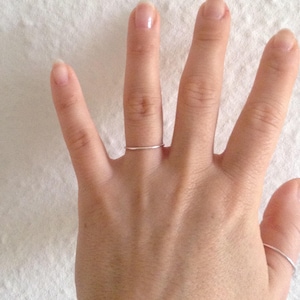 May include: A close-up of a hand wearing two thin silver rings on the ring finger.