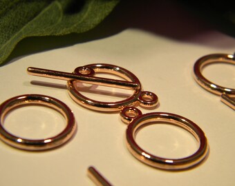 May include: Rose gold metal toggle clasp with two round rings. The toggle clasp has a bar that slides through the rings.
