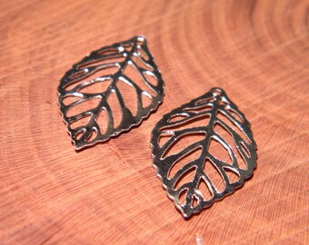 May include: Two silver-colored leaf-shaped charms with intricate vein detailing. The charms are displayed on a wooden surface, showcasing their delicate design. These charms are ideal for jewelry making or craft projects.