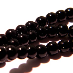 May include: A strand of black beads, strung together to form a necklace or bracelet. The beads are round and smooth, and they have a glossy finish.