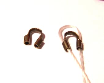 Puede incluir: Dos cuentas de crimpado de metal dorado, una en un cordón blanco, utilizadas para la elaboración de joyas.