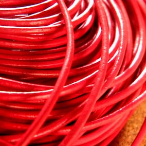 Puede incluir: Primer plano de un carrete de cordón de cuero rojo brillante. El cordón está enrollado apretado y tiene un acabado liso y brillante.