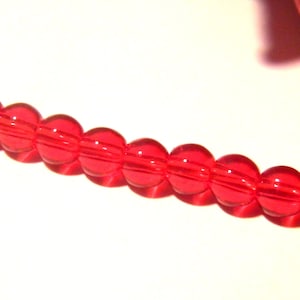 May include: A strand of bright red glass beads. The beads are round and have a slightly textured surface.