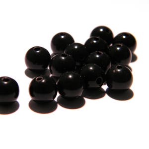 Peut inclure: Un groupe de perles rondes noires, éparpillées sur une surface blanche.