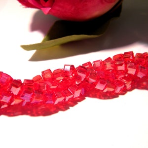 Puede incluir: Una hebra de cuentas cuadradas rojas iridiscentes, dispuestas en un patrón ondulado sobre una superficie blanca.