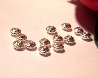 May include: A collection of silver-toned metal beads with a raised design. The beads are arranged on a white surface.