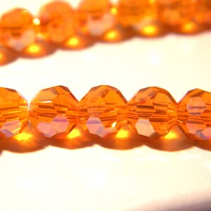 Può includere: Una collana di perline di vetro sfaccettate arancioni. Le perline sono infilate su un filo trasparente.