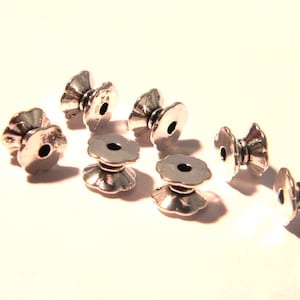 May include: A set of eight silver metal bead caps with a decorative flower design. The caps have a hole in the center for threading.
