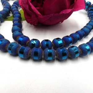 May include: A strand of blue and iridescent glass beads with a metallic finish. The beads are round and have a textured surface.