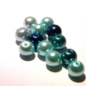 Peut inclure: Un ensemble de perles irisées dans les tons de turquoise, d'argent et de bleu marine. Les perles sont rondes avec une finition brillante, et chacune a un petit trou. Les perles sont disposées en grappe, certaines se chevauchant.