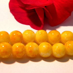 May include: A strand of yellow and white beads with a marbled effect. The beads are round and smooth.