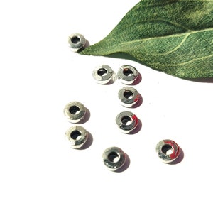May include: A group of ten silver-toned metal spacer beads, each with a round hole in the center. The beads are scattered on a white surface.