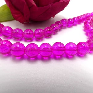 May include: A strand of bright pink glass beads with a textured surface. The beads are round and have a slight shimmer.