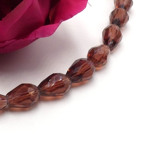 May include: A strand of brown faceted teardrop glass beads. The beads are strung on a clear thread.