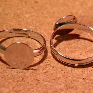 May include: Two silver adjustable rings with round, flat, silver-coloured metal bases. The bases are smooth and appear to be for attaching a design or image.