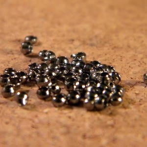Peut inclure: Gros plan sur un tas de perles métalliques de couleur argent. Les perles sont petites et rondes, et elles sont disposées de manière aléatoire. Il y a une perle légèrement plus grande que les autres, qui est sur le côté.