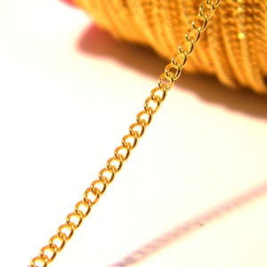 Peut inclure: Gros plan sur une chaîne dorée, montrant les maillons individuels. La chaîne est posée sur une surface blanche.