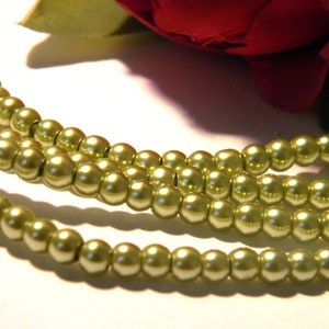 Peut inclure: Un brin de perles de couleur vert clair, disposées en trois rangées, sur une surface blanche.