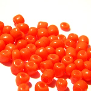 May include: A large pile of bright orange round beads. The beads are made of glass and have a smooth, shiny finish.