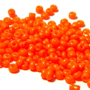 May include: A large pile of bright orange seed beads. The beads are small and round, and they are all the same size.