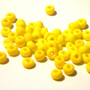 May include: A large group of bright yellow round beads, scattered on a white surface.