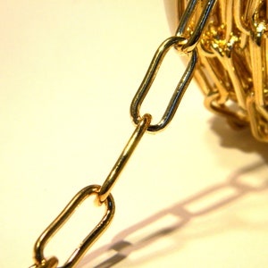 Può includere: Primo piano di una catena d'oro, che mostra i singoli anelli. La catena è su una superficie bianca.